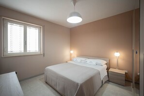 A bedroom with a bed, bedside lamps, a nightstand, a window with curtains, and a ceiling light.