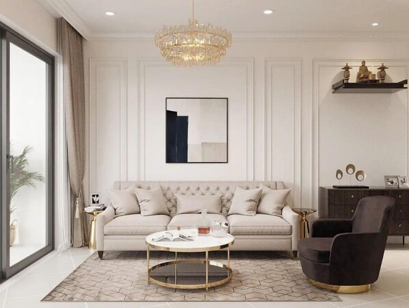 Un salon moderne avec un canapé, une table basse ronde, un fauteuil sombre, un lustre et une œuvre d’art encadrée accrochée au mur.