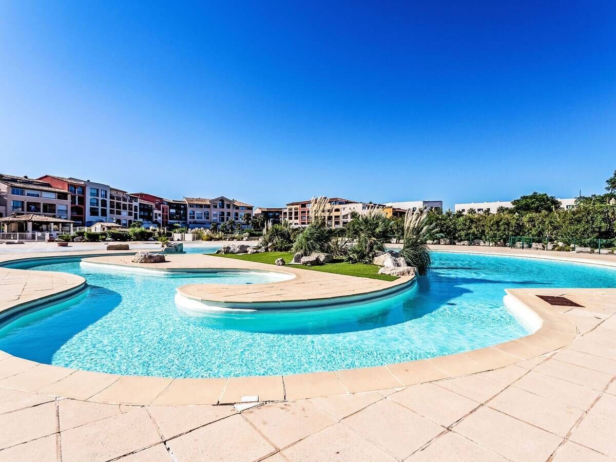 A swimming pool with a curved design, surrounded by a tiled deck and greenery.