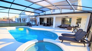 Un área de piscina moderna al aire libre con un porche de vidrio, sillas de descanso y un jacuzzi.