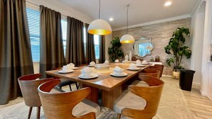 Un comedor con una larga mesa de madera dispuesta para una comida, rodeada de sillas de madera con asientos acolchados.
