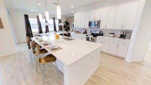 Una cocina moderna con armarios blancos, una isla grande y taburetes de bar.