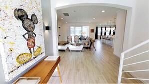 Amplia sala de estar con diseño moderno, que presenta un cuadro abstracto grande en la pared, un banco de madera y una zona de comedor con sillas y una mesa.