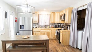 A modern kitchen with wooden cabinets, stainless steel appliances, and a wooden dining table. - Remodeled cabin. New Central Air… (Ruidoso)
