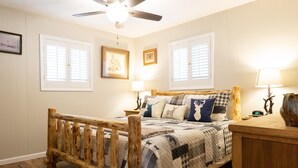 A bedroom with a wooden bed, two bedside lamps, a ceiling fan, and two windows with shutters. - Remodeled cabin. New Central Air… (Ruidoso)
