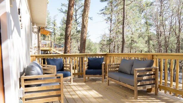 A wooden deck with outdoor seating, surrounded by tall trees. - Remodeled cabin. New Central Air… (Ruidoso)