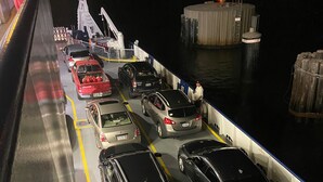 Un ferry con coches estacionados en filas, un muelle y un pequeño edificio con una luz en la parte superior.