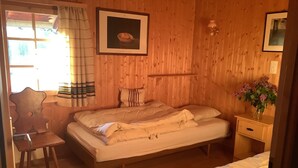 A wooden-paneled room with a bed, a chair, a nightstand, and a framed picture on the wall.