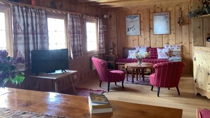 A cozy cabin interior with wooden walls, a sofa set, a television, and a dining table.