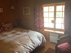 Un dormitorio con cama, una silla, un radiador, una ventana con cortinas y un cuadro en la pared.