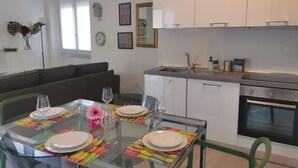 Une cuisine moderne avec des meubles blancs, un four en acier inoxydable et un coin repas doté d’une table en verre, mise pour quatre personnes.