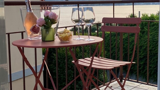 Un balcon avec une table dressée pour deux personnes, agrémentée d’une bouteille de champagne, d’un vase rempli de fleurs et d’un bol de collations.