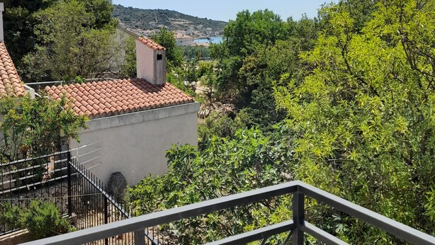 Une terrasse dotée d’un toit en tuiles, entourée de verdure et offrant une vue lointaine sur une ville.