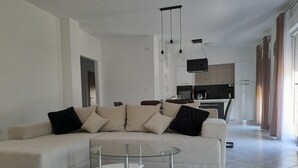 Un salon moderne avec un canapé d’angle, une table basse en verre et une cuisine en arrière-plan.
