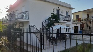 Un bâtiment à deux étages, à l’extérieur blanc, doté d’un balcon avec une rambarde en métal et d’un petit patio aménagé avec du mobilier d’extérieur.
