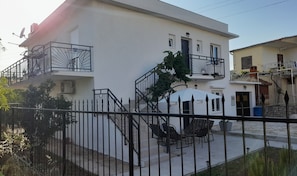 A two-story building with a white exterior, a balcony with a metal railing, and a small patio area with outdoor furniture.