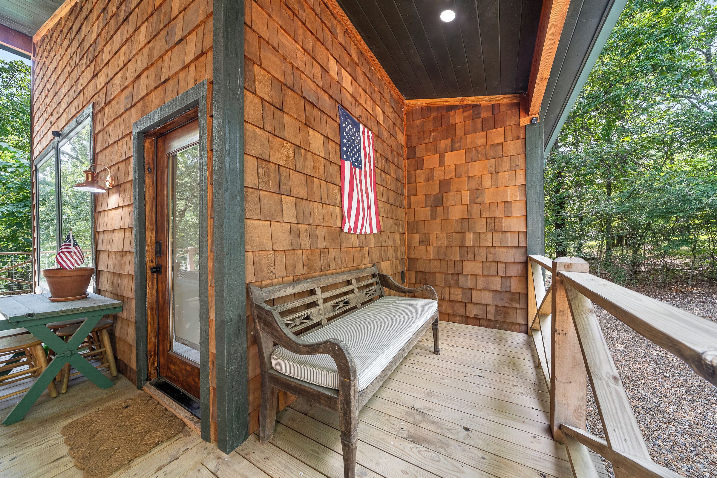 A wooden deck with a bench and a table, an American flag, and a door.