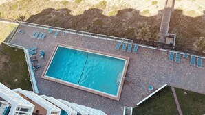Vista aérea de una zona de piscina con una pileta rectangular, varias sillas de descanso y un muelle de madera.