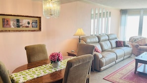 A living room with a dining table, chairs, a sofa, and a lamp.