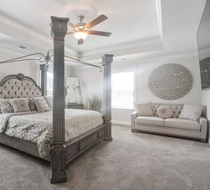 A bedroom with a four-poster bed, a ceiling fan, a large round wall decoration, and a sofa.