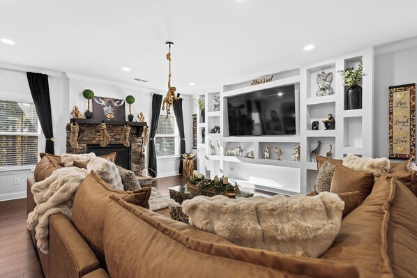 A modern living room with a brown sofa, a fireplace, and a TV wall unit.
