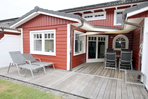 Uma casa vermelha com deck de madeira, duas cadeiras de descanso e uma mesa.