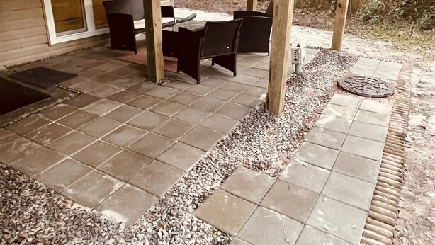 Un portico coperto con un tavolo e sedie, circondato da un muretto in legno e un pavimento in pietra.