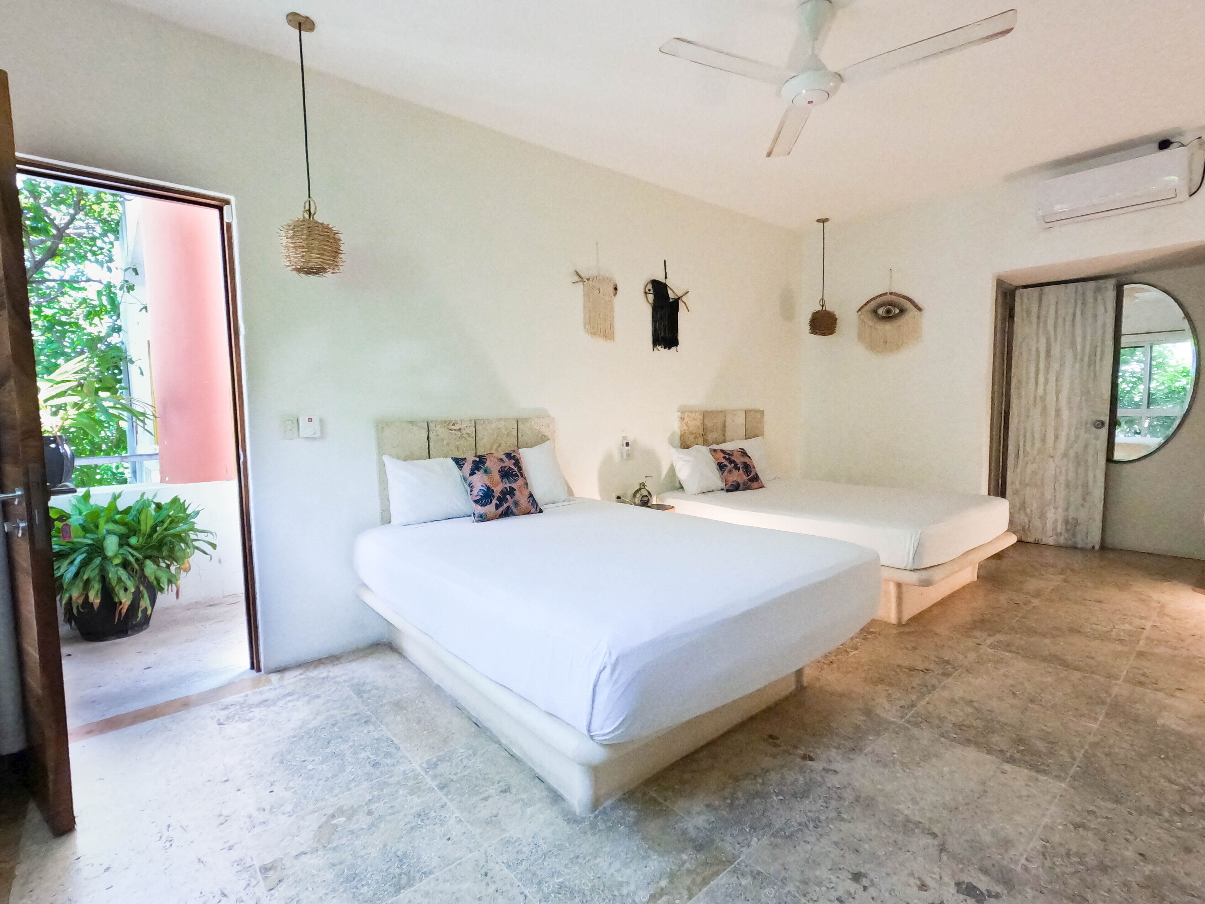 A bedroom with two beds, a ceiling fan, a potted plant, and a view of the outdoors.