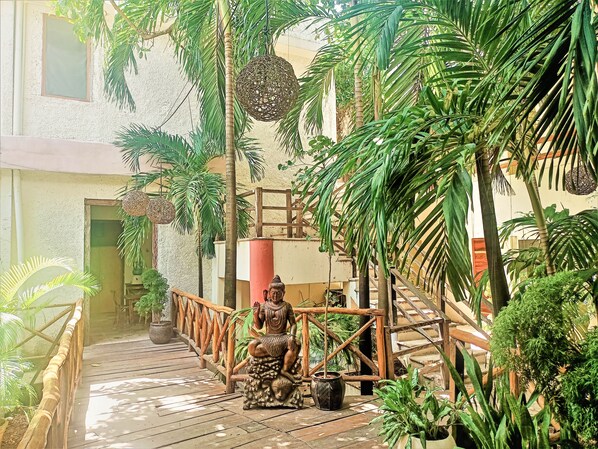 A wooden bridge, a statue, and lush greenery in a courtyard. - Rustik-inn (Playa del Carmen)