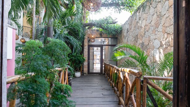 A wooden pathway with a railing, surrounded by lush greenery and a stone wall. - Rustik-inn (Playa del Carmen)