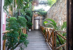 A wooden pathway with a railing, surrounded by lush greenery and a stone wall. - Rustik-inn (Playa del Carmen)
