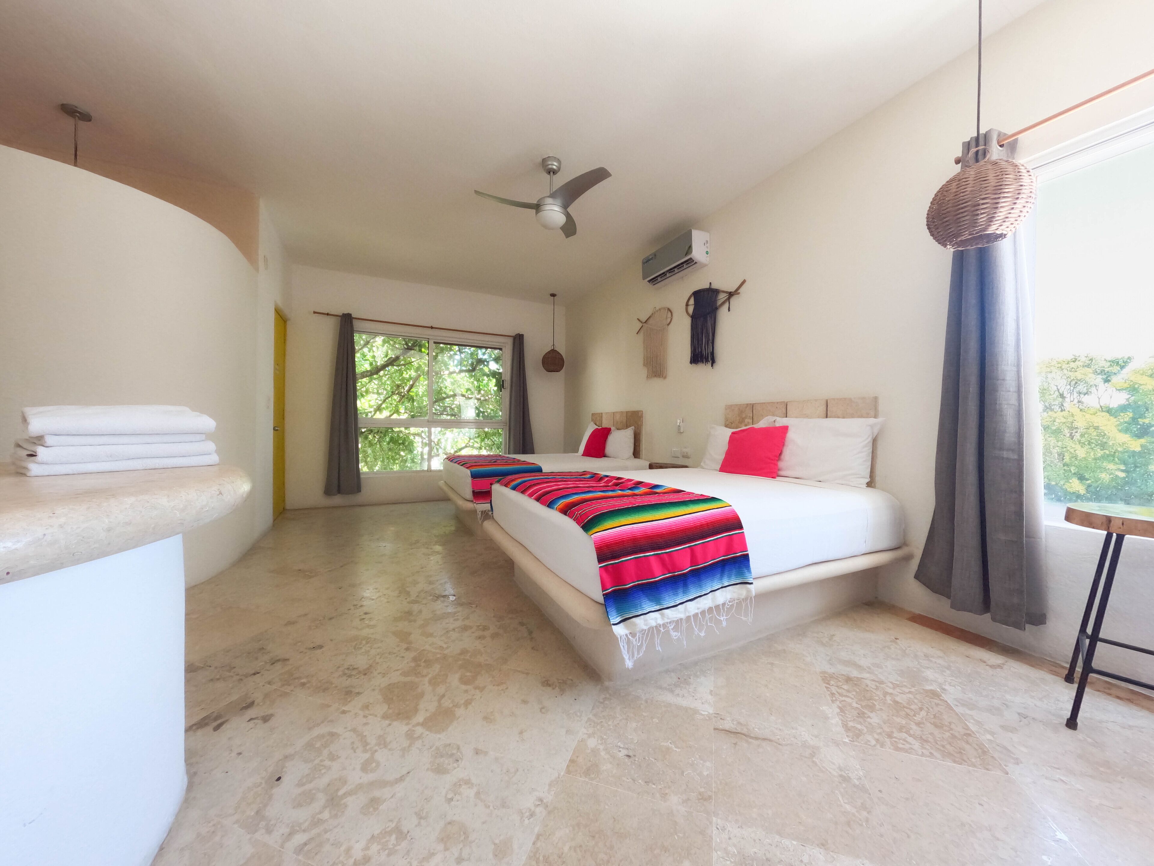 A bedroom with two beds, a ceiling fan, a window with curtains, and a view of trees.