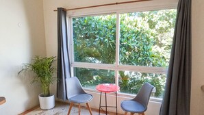 A room with a large window, two chairs, a small table, and a potted plant. - Rustik-inn (Playa del Carmen)