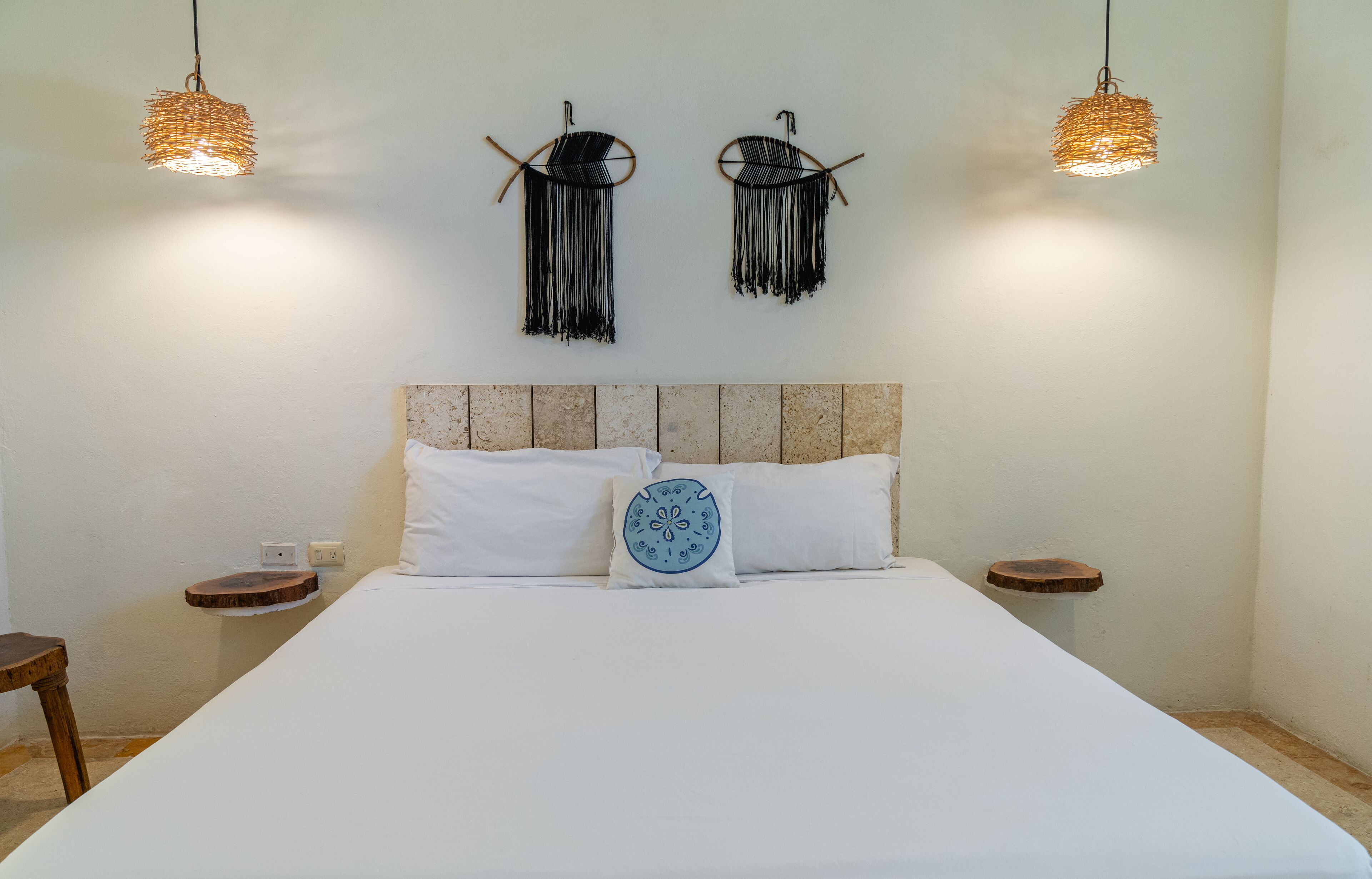 A bedroom with a large bed, two bedside tables, a headboard, and two hanging lamps.