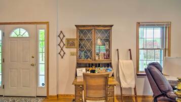 Une pièce comprenant un bureau en bois, une chaise en osier, un meuble avec des portes en verre, une fenêtre et une porte.