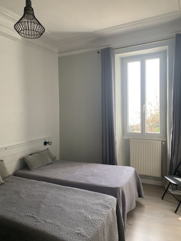 Una habitación con dos camas, un radiador, una ventana con cortinas y una lámpara colgante.