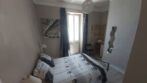 Un dormitorio con cama, lámpara de noche, ventana con cortinas, espejo y lámpara colgante.