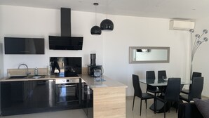Una cocina moderna con una isla central, horno integrado y armarios negros. Hay un comedor con una mesa de vidrio y sillas negras.