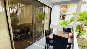 A modern outdoor dining area with a glass sliding door leading to a patio, a table with chairs, and potted plants. - Hilo SunShine Rental.2bds1ba,common swimming pool. (Hilo)
