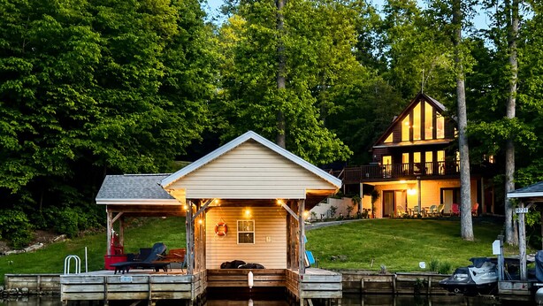 A lakeside cabin with a dock, a covered seating area, and a larger building in the background. - Updated Lakefront Retreat, Fiber WiFi, Fire Pit, 15 Min to VIR (Leasburg)