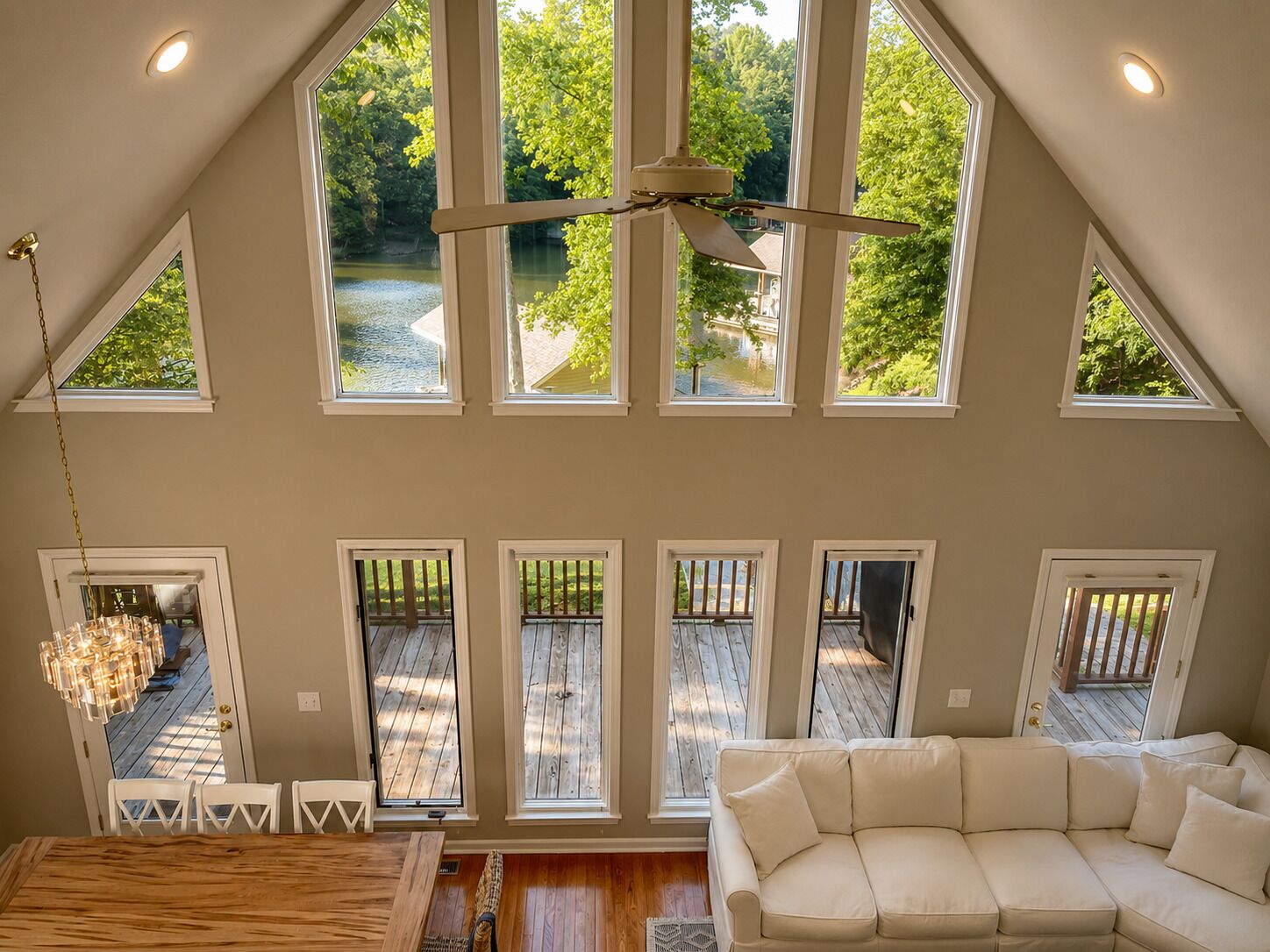 Un loft spacieux avec un plafond haut, de nombreuses fenêtres donnant sur une zone boisée, un ventilateur de plafond et un coin salon confortable.
