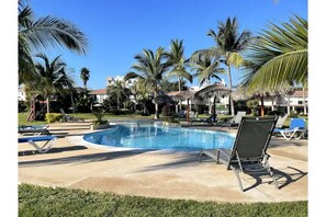 Relax by the resort pool surrounded by palm trees and lounge chairs.