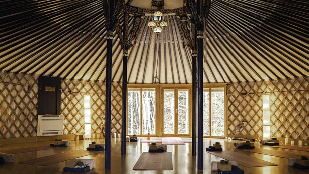 A spacious interior with a high ceiling, wooden beams, and a central chandelier. There are yoga mats arranged on the floor, and a large window provides natural light. - The Glowbug Cottage (Morell)
