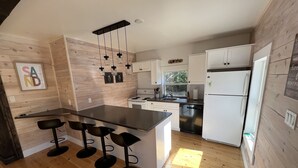A modern kitchen with wooden walls, a central island with bar stools, a refrigerator, and a dishwasher. - The Glowbug Cottage (Morell)