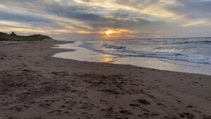 A beach with footprints and waves, a house on the left, and a sunset. - The Glowbug Cottage (Morell)