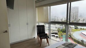 Ein Schlafzimmer mit großem Fenster, einem Bett, einem Sessel und einem Kleiderschrank.