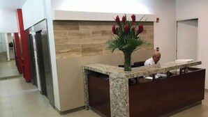 Ein Empfangsschalter mit einer Vase roter Blumen, einer Marmorplatte und einer Wand aus Stein im Hintergrund.
