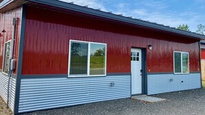 A red and grey metal building with two windows and a door. - Upper Mesa Villa #11, Glacier Suites - Upper Mesa Villa #4 (Matanuska-Susitna)