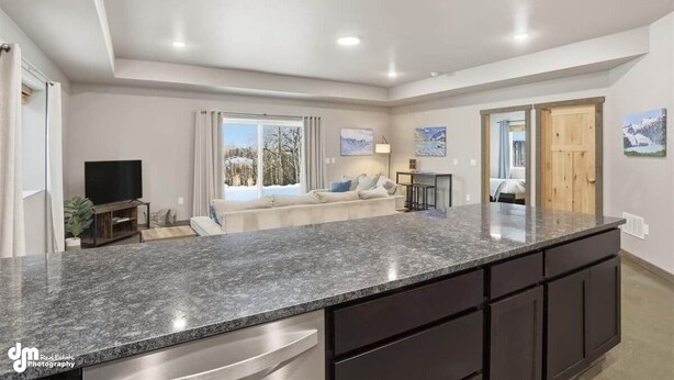 A spacious kitchen with granite countertops, a built-in oven, and a dining area with a table and chairs. - Upper Mesa Villa #11, Glacier Suites - Upper Mesa Villa #4 (Matanuska-Susitna)