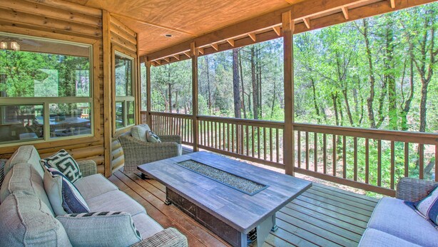 Una terraza de madera con un sofá y una mesa, con vistas a un bosque.